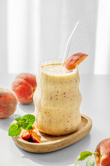 Smoothie with peach and banana in a glass on a wooden board on a white table near window