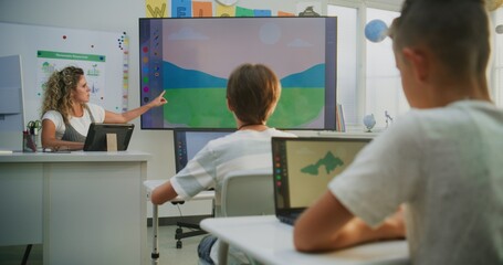 Female Teacher Teaching Young Kids During Art Lesson Using Tablet Computer and Digital Screen. Primary School Students Creating Digital Drawings on Laptops. STEM Learning for Creativity, Imagination.