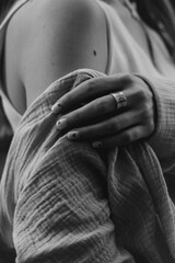 A black and white close-up captures a woman's hand with a detailed ring resting on her shoulder, evoking quiet strength and intimacy