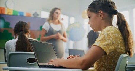 Primary School Girl Creating Illustration on Laptop, Practicing Digital Skills in Modern Classroom. Female Teacher Guiding Young Kids During Art Lesson Using Digital Screen. Creative STEM Learning.