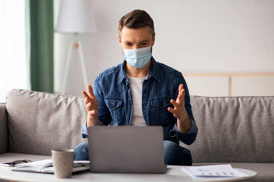 Businessman in protective face mask having online conference with business partners from home during coronavirus pandemic, middle-aged man sitting on couch and using laptop, free space - Powered by Adobe