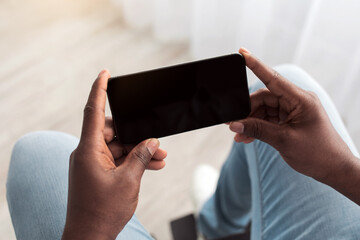 Spare time during covid-19 quarantine, entertainment and video online on devise. Middle aged african american guy disabled in wheelchair holding smartphone with empty screen in living room interior