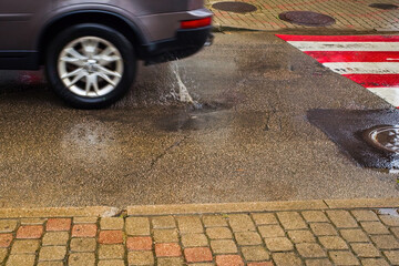 Obraz premium Car driving through a puddle on wet asphalt near pedestrian crossing
