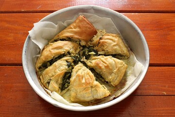 Golden, flaky spanakopita pie in a round pan on a wooden table