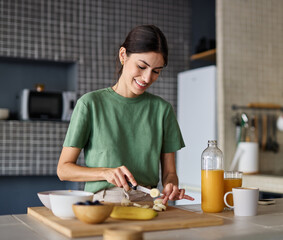Portrait of a young woman preparing and eating breakfast, drinking juice in the kitchen at home