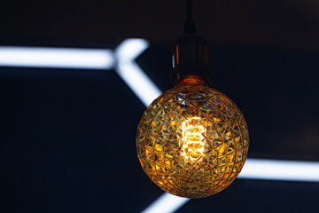 A decorative incandescent light bulb hangs from a dark ceiling.