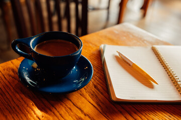 cup of coffee on wooden table with open notebook and yellow pen