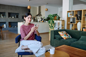 Portrait of a young latina woman chatting with boyfrien at home, using modern mobile phone,...