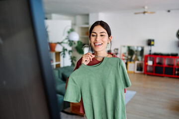 Woman choosing between green and brown shirt in closet in  living room