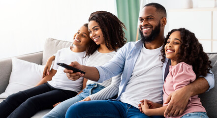 Comfort And Relax. Portrait of happy loving black family of four people watching tv, smiling...