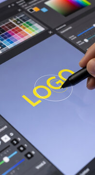 Stylus creating yellow logo on digital tablet screen, surrounded by design tools, showcasing graphic design process, ideal for branding or technology concepts