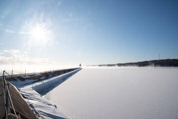 Snow-covered pier leading to lighthouse on frozen Lake Superior