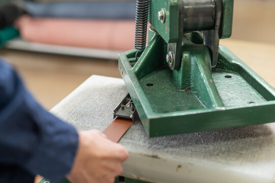 A woman makes holes in a leather belt in a workshop.