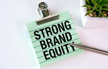 A clip board with the words Strong Brand Equity written on it. A pen is sitting on top of the clip...