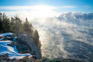 Sunrise over Lake Superior cliffs with steam fog and snowy forest