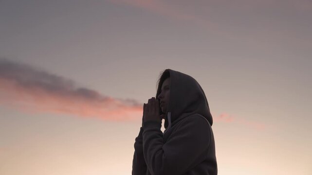 a girl prays at sunset, happy man asks for forgiveness from heaven, repent of evil deeds, read prayer before bedtime, believing woman thinks about good and kind life, looking up with her palms folded.