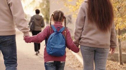 small child with backpack holds mother and father by hand, kid with mom and dad walks around schoolyard after school, happy family, rush to first call, primary education, school bag on baby shoulders.
