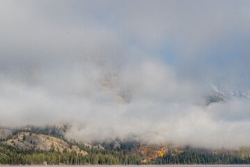 Low clouds partially obscure the rugged mountains in Grand Teton National Park, Wyoming, creating a misty veil over the landscape.