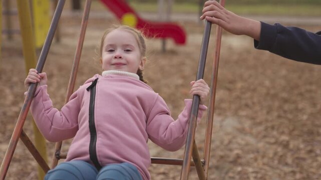 little girl swinging on swing autumn park, child with her mother is having fun vacation on playground, happy family, kid smiling while playing outside, autumn nature with yellow leaves, cheerful baby.