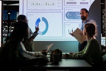 Team of business analysts exchanging project details and forecast data to help achieve business...