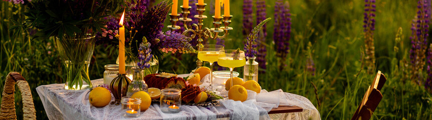 Banner. Summer vacation, marriage proposal, date or wedding concept. Romantic sunset dinner in a meadow. Table honeymoon set for two with gourmet food, glasses of limoncello. Garden party arrangement