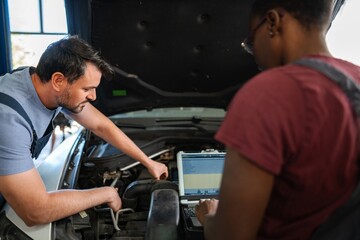 Two mechanics repairing a car engine using a computer diagnostic software