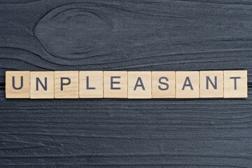 text on word unpleasant from gray wooden letters on a black background
