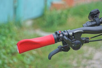 part of a black metal bicycle handlebar with a handbrake and a red plastic handle on a background...