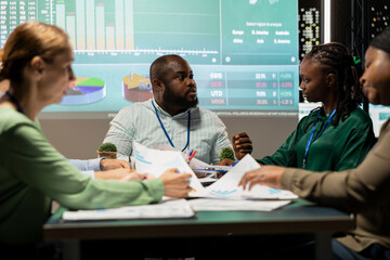 Diverse employees discuss project details and forecast information at night, ensuring business...