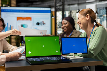Determined diverse corporate team using display with chroma key, exchanging reports and strategy insights with data visualization. Work environment and productivity in office workspace.