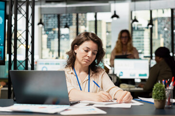 Businesswoman evaluates key performance metrics and writes reports at her desk, planning financial strategy with her analytical mindset. Professional leadership in business activity.