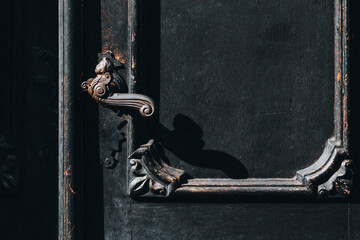 Ornate antique door handle on dark wooden panel with shadow