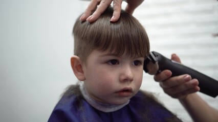 a three-year-old child curiously watches himself in the mirror while a barber gently cuts his hair in a cozy kids salon