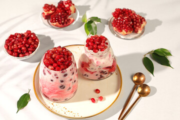 Fruit yogurt with pomegranate seeds and fresh cow cream for healthy nutrition in a glass on an elegant table. Healthy breakfast with ingredients, kitchen background