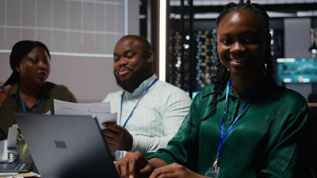Portrait of smiling black analyst preparing a pitch for important meeting, increasing funds for development after hours. Coworkers team attend a discussion to address goal setting. Camera A.