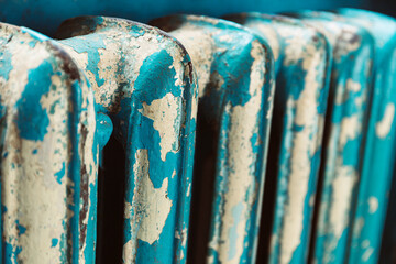 Close-up of an old cast iron radiator with peeling turquoise and beige paint. The rustic texture,...