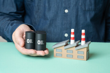 A man holds oil barrels toward an industrial plant. Providing industry with energy resources. Power...