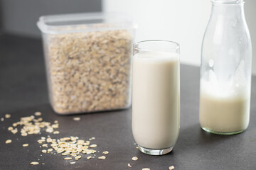 A glass of oat milk and oatmeal in a box on grey kitchen table. Vegan and non-dairy alternative milk