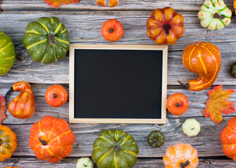 Top view chalkboard surrounded by mini pumpkins and autumn leaves on table, copy space