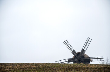 Traditional wooden windmill against a gray, overcast sky. The windmill is seen from a low angle,...