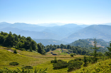 Mountain landscape with multiple layers of rolling hills and peaks fading into soft blue haze. Lush...