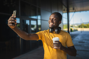 Smiling young man taking selfie while holding coffee outside office building