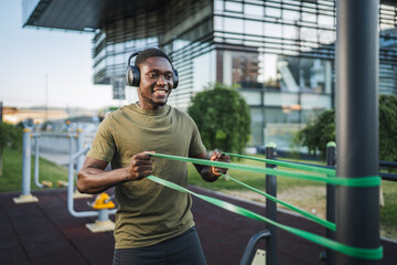 Young sportsman exercising with resistance band listening to music with headphones