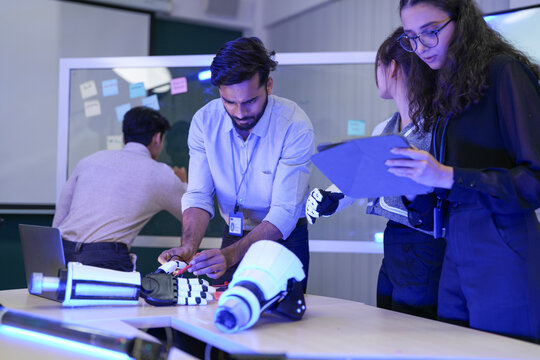 A multidisciplinary team in an agile R&D session for a bionic limb. They assemble prototypes while analyzing real-time biomechanical data, integrating hardware with a predictive AI.