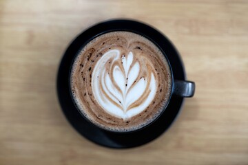 Coffee latter art in a black cup, flatlay top view on brown wooden table