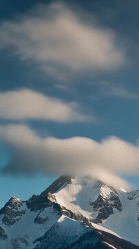 Vertical 9:16 cinematic video of time-lapse clouds moving quickly across snow-covered mountain peaks, cool tones, realistic landscape.
