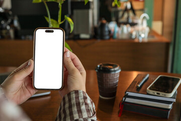 Close-up of female hands holding smartphone with blank screen at cafe table with coffee cup and notebooks