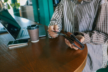 Close-up of woman holding wallet with bank card at cafe table, laptop, smartphone, and coffee cup...