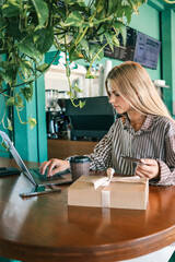 Young woman making online payment with credit card while using laptop in cafe, gift box and coffee...