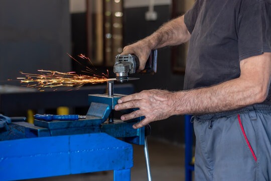 The locksmith cuts off the metal, clamped in a vice, with a grinder with a cut-off wheel. Sparks from metal polishing by the grinder. - Powered by Adobe